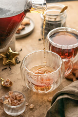 Pouring black tea into transparent glass cup from teapot on brown textured table background. Frozen spalshes of tea in cup