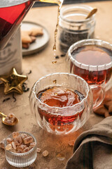 Pouring black tea into transparent glass cup from teapot on brown textured table background. Frozen spalshes of tea in cup