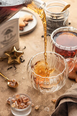 Pouring black tea into transparent glass cup from teapot on brown textured table background. Frozen spalshes of tea in cup