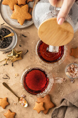 Black tea in two transparent glass cups on brown textured table background with teapot, cookies and ingredients. Pouring tea process, teatime, top view
