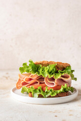 Delisious sandwich with ham lettuce tomatoes and grilled bread for breakfast on beige kitchen table, copy space