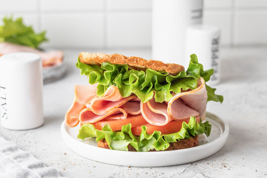 Delisious sandwich with ham lettuce tomatoes and grilled bread for breakfast on white kitchen table
