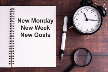 Minimal workspace with notebook, inspirational quote, classic alarm clock, pen, and magnifying glass on wooden desk for motivation and productivity themes.