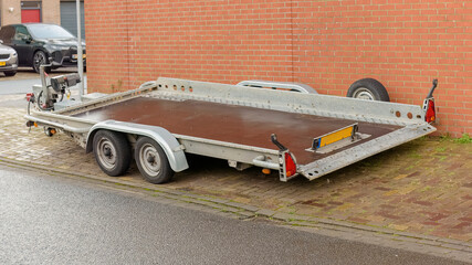 two axle trailer is parked outside on the street next to a stone wall
