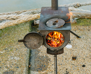 rusty metal portable wood stove with open round door showing the flames and burning wood