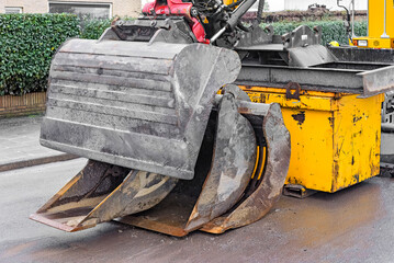 steel digging buckets and an excavator are outside on the asphalt