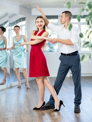 Naklejka premium Smiling elegant young adult couple, bride and groom rehearsing sensual wedding dance in studio under guidance of professional female choreographer in bright studio..