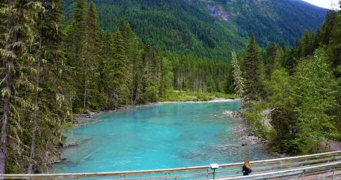 Aerial footage of a woman crossing a wooden bridge along the Berg Lake Trail near Kinney Lake. The drone flies above as the turquoise Robson River rushes below, surrounded by pristine wilderness.