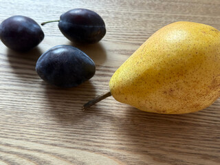 Composition of fresh plums and a ripe pear on a wooden table in soft daylight. The scene evokes healthy eating and rustic charm. Suitable for food blogs, recipe books, or healthy lifestyle themes