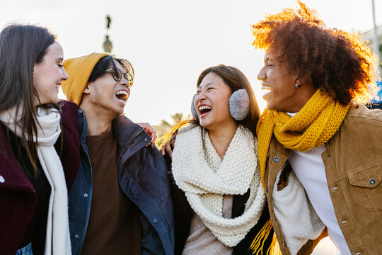 Diverse group of young friends having fun together outdoors on winter. Millennial student people laughing walking in city street enjoying day off. Youth community and friendship concept.