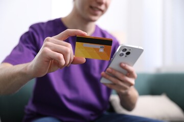 Young man making online payment with phone and credit card indoors, closeup