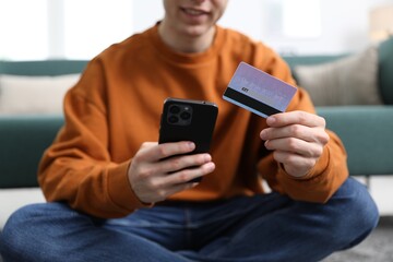 Young man making online payment with phone and credit card indoors, closeup