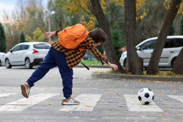 Little boy with backpack catching ball on pedestrian crossing outdoors. Child in danger and road safety