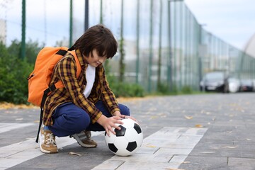 Little boy with backpack and ball on pedestrian crossing outdoors, space for text. Child in danger and road safety