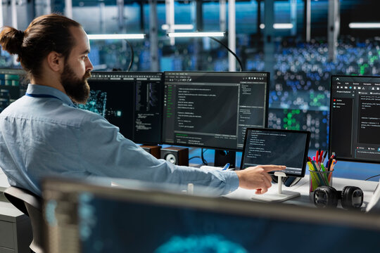 Data center system administrator using tablet, coding, managing systems for uptime and efficiency. IT employee pressing device touchscreen, using programming languages in server hub