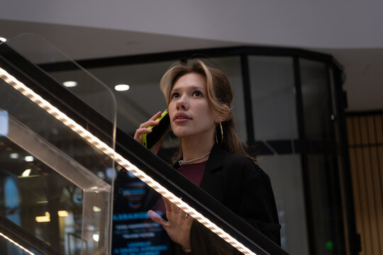 Young woman talking on smartphone while riding escalator in shopping mall - Powered by Adobe
