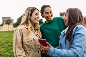 Three young female friends having fun using smart phone outside. Social media and communication lifestyle concept
