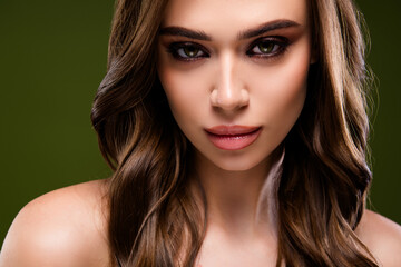 Fototapeta premium Portrait of a beautiful young woman with long brunette hair and flawless makeup posing against a green background