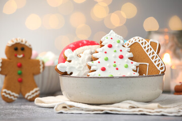 Tasty gingerbread cookies, marshmallows and burning candle on grey table against Christmas lights,...
