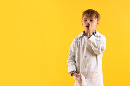 Cute little boy in laboratory coat and protective goggles on yellow background, space for text. Child and science