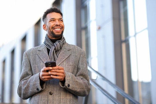 Smiling man in suit with smartphone on city street, low angle view. Space for text - Powered by Adobe