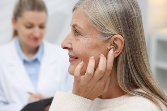 Senior woman with hearing aid having appointment with doctor in clinic, selective focus