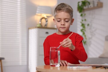 Cute little boy painting at wooden table indoors. Space for text