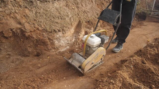 worker operating trench compactor, operator in boots manages trench compactor for foundation work, underground worker operating plate compactor to prepare soil for building foundation