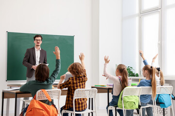 Children raising hands to answer teacher's question in classroom