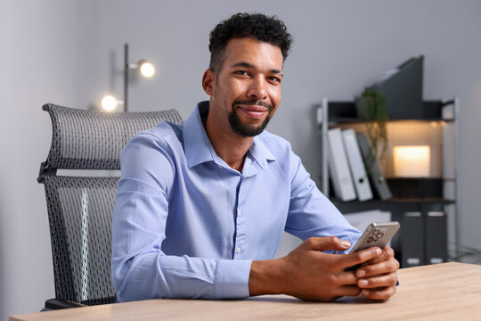 African-american man using smartphone at wooden table indoors