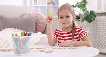 Fototapeta premium Little girl learning alphabet with letters at white table indoors