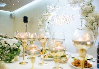 Close-up of elegant wedding head table with floating candles in gold holders and white floral arch with love sign in the background