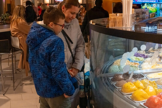 Mother and son choosing ice cream flavors at gelato display counter in busy cafe looking at colorful varieties. Concept of family dessert outing, sweet treat selection and parent child bonding moment. - Powered by Adobe