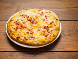 German pizza style dish with ham, potato, cheese and creamy sauce on a wooden table. Popular and tasty dish. Simple dinner.