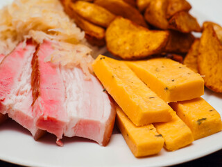 Plate with smoked ham, spicy potato wedges, cheese and sour cabbage. Tasty dish, Big portion of food. Pork meat sliced in fine portions.