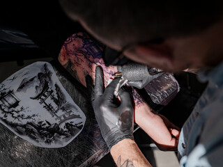 Tattoo artist working on Japanese sleeve in dramatic studio lighting with reference stencil visible in foreground.