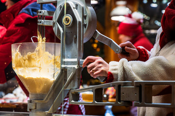 Close view of a vendor operating a dough funnel machine at a christmas market food stall. Batter is being prepared and portioned at festive kitchen
