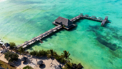 Aerial view of a tropical resort with a long pier over turquoise water and people swimming.