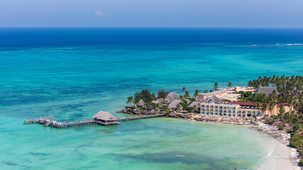 Aerial view of a tropical resort with a long pier over stunning turquoise ocean.