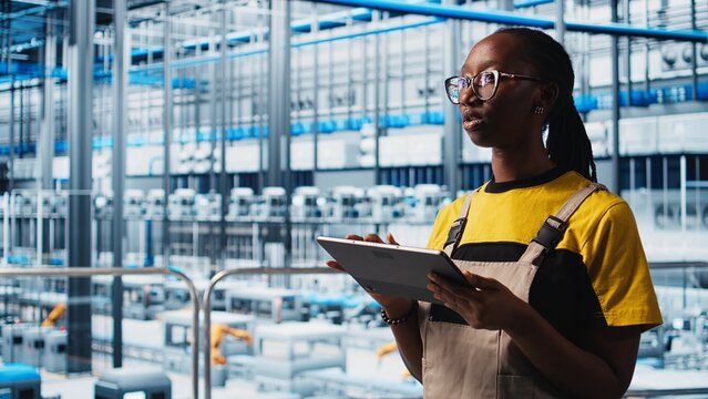 Industry 4.0 plant technician monitors system performance using digital device app. Smart factory engineer oversees operation of robotic arms and conveyor belts using software on tablet, camera A