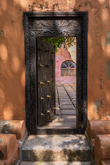 Ornate wooden door in an old orange wall opens to a sunlit courtyard.