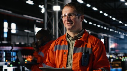 Engineer oversees assembly tools on tablet in industry plant, surrounded by metal and steel...