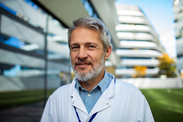 Mature doctor smiling outside modern hospital