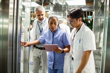 Adult and mature medical team focused on tablet in hospital elevator
