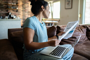 Young adult woman reviewing bills on laptop at home, worried