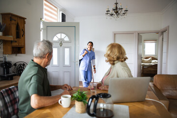 Young caregiver greeting senior couple in home kitchen, cheerful