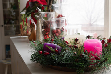 Unlit advent wreath on a white sideboard with christmas decorations by window
