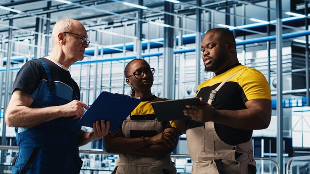 Industry 4.0 photovoltaics plant senior engineer reading paperwork talks with workers to maximize power generation. Solar panels smart factory experienced leader giving tasks to technicians, camera A