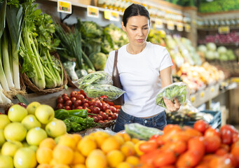 Adult woman buyer choosing fresh green onions in vegetable shop