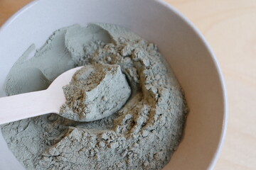 Close-up of a bowl of green clay with a wooden spoon. A wooden spoon with gren clay. Healing with green clay. Skin mask with green clay.